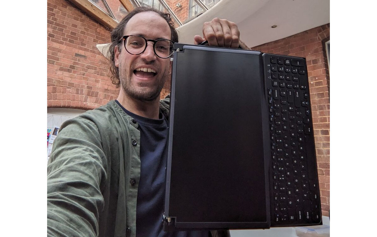 Picture of engineer holding the Canute Scientific up by its side handle. A full size keyboard in the front. Behind this the lid is closed over the Braille display.